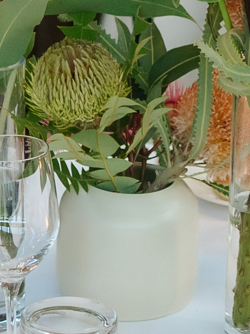 Floral arrangement in a white vase on a table with glasses and a white background